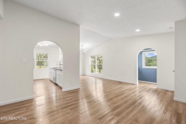 unfurnished living room with a healthy amount of sunlight, arched walkways, and light wood finished floors