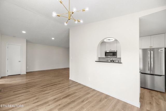 kitchen with appliances with stainless steel finishes, baseboards, white cabinets, a chandelier, and light wood-style floors