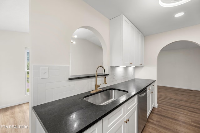 kitchen with arched walkways, tasteful backsplash, dishwasher, a sink, and light wood-style flooring