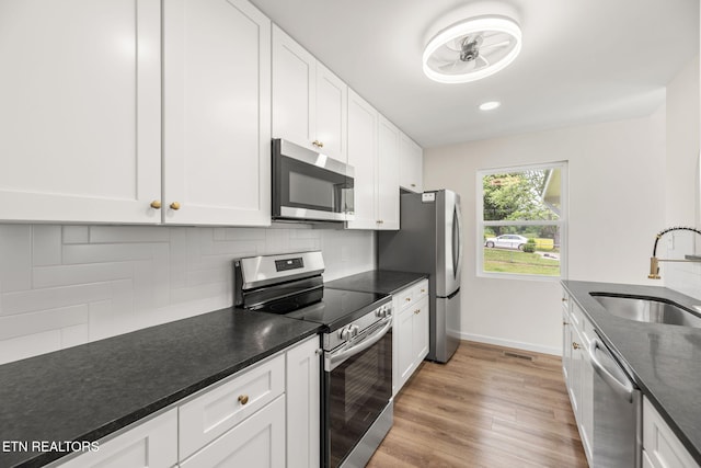 kitchen with dark countertops, a sink, stainless steel appliances, white cabinetry, and backsplash