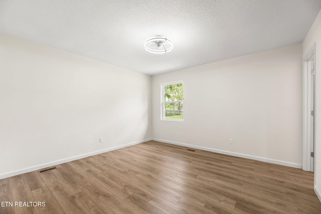 spare room with baseboards, a textured ceiling, wood finished floors, and visible vents