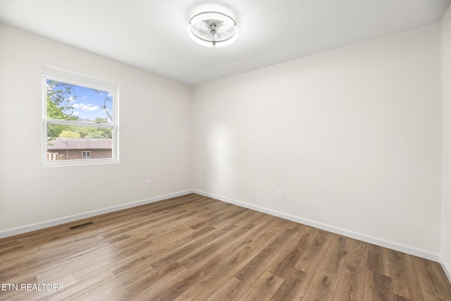 spare room with baseboards, visible vents, and wood finished floors