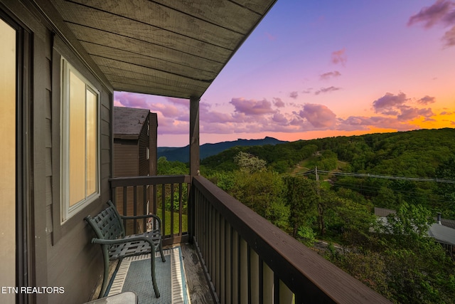 balcony at dusk featuring a wooded view