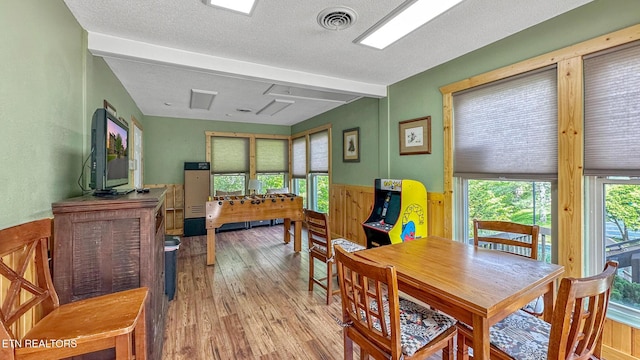 dining area featuring wood-type flooring, wainscoting, a textured ceiling, wooden walls, and beamed ceiling