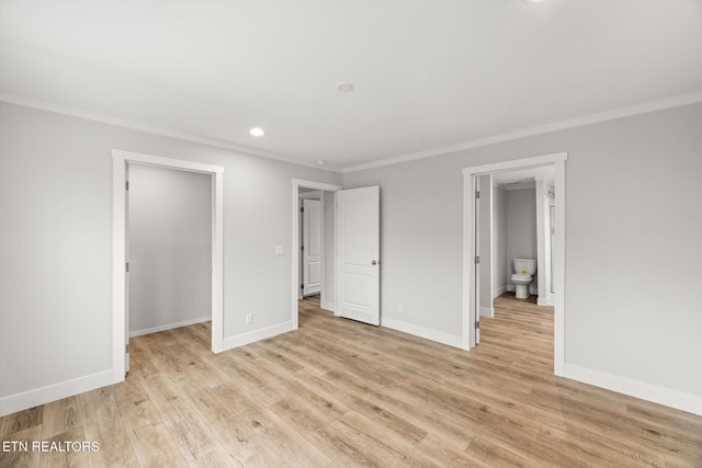 unfurnished bedroom with baseboards, ornamental molding, a walk in closet, and light wood finished floors