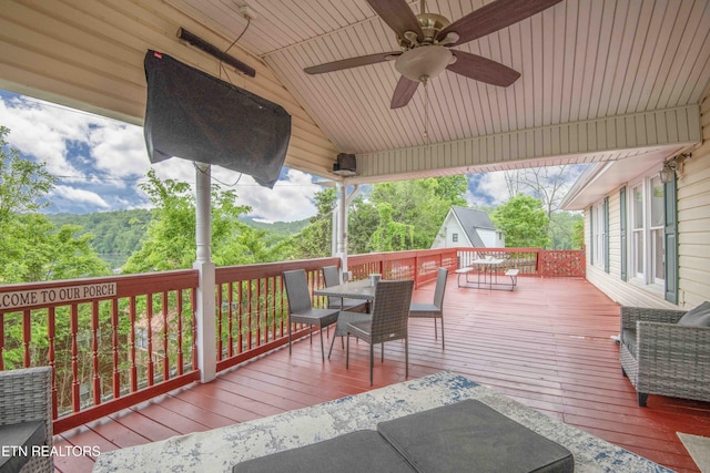 wooden deck featuring outdoor dining space, ceiling fan, and an outdoor structure