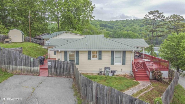 bungalow-style house featuring metal roof, a wooded view, an outdoor structure, a fenced backyard, and a storage unit