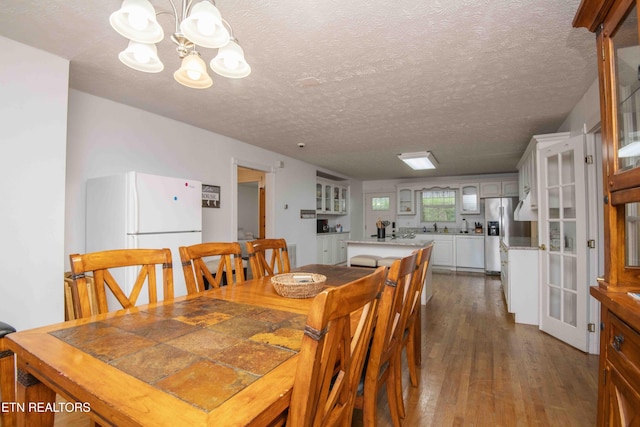 dining area with a textured ceiling, a notable chandelier, and dark wood-type flooring