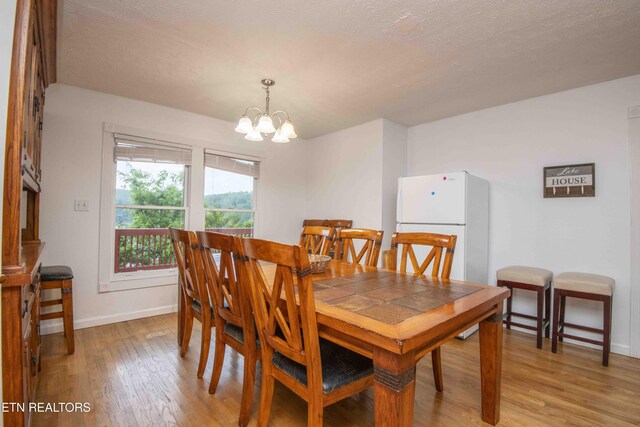 dining space with baseboards, a textured ceiling, light wood-style flooring, and a chandelier