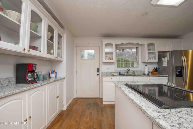 kitchen with wood finished floors, black electric cooktop, white cabinets, stainless steel fridge with ice dispenser, and a sink