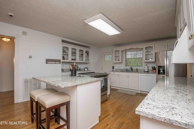 kitchen with a sink, appliances with stainless steel finishes, a kitchen island, and light wood-type flooring