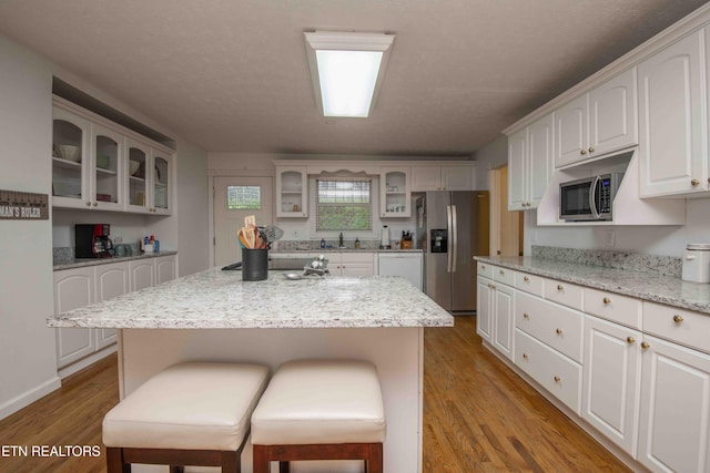 kitchen with a kitchen bar, appliances with stainless steel finishes, wood finished floors, a sink, and glass insert cabinets