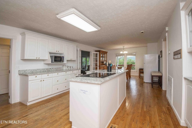 kitchen with freestanding refrigerator, light wood-style floors, black electric stovetop, white cabinetry, and stainless steel microwave