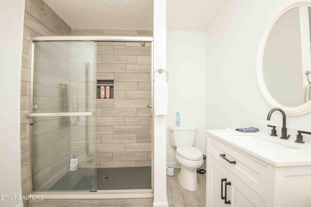 bathroom with vanity, a shower stall, toilet, and a textured ceiling