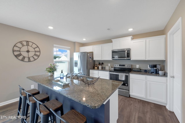 kitchen with a kitchen breakfast bar, a sink, dark wood-style floors, dark stone countertops, and stainless steel appliances