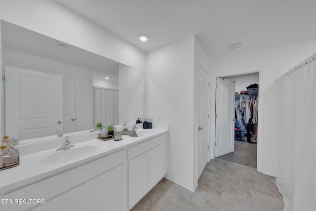 full bath featuring a sink, a walk in closet, baseboards, and double vanity