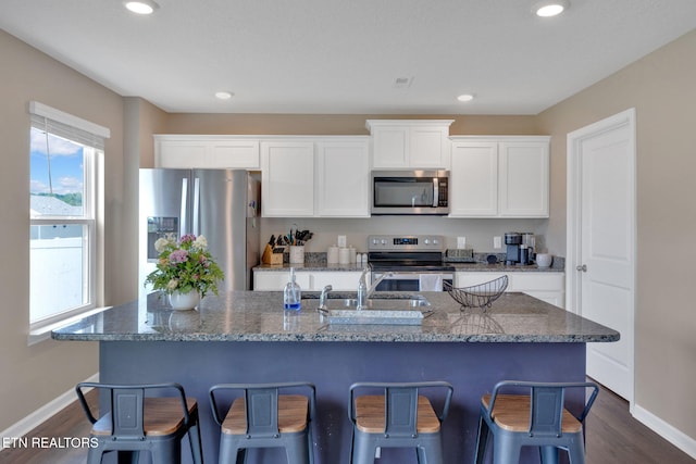 kitchen with dark wood-style flooring, stainless steel appliances, baseboards, and an island with sink