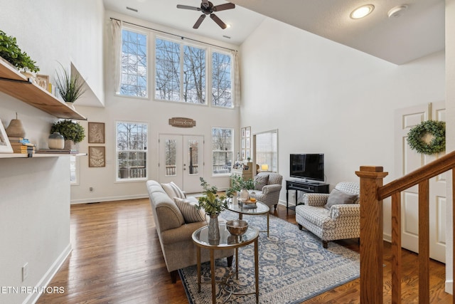living room featuring baseboards, a ceiling fan, a towering ceiling, and wood finished floors
