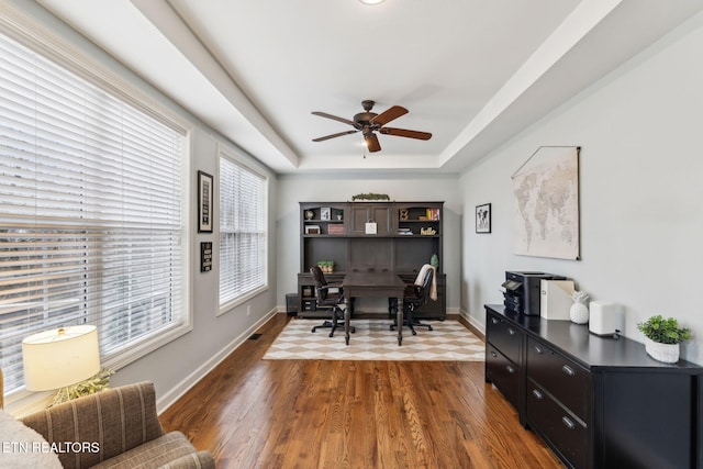 office area with a tray ceiling, baseboards, a ceiling fan, and dark wood-style flooring