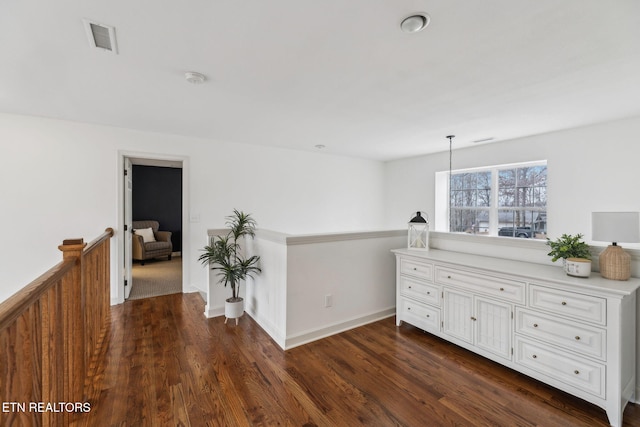 hallway with visible vents, baseboards, dark wood-style floors, and an upstairs landing