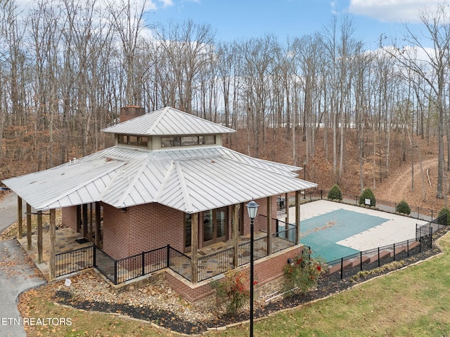 rear view of property with fence, brick siding, a fenced in pool, a patio, and metal roof