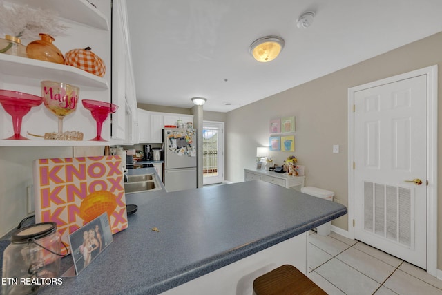 kitchen featuring open shelves, freestanding refrigerator, a peninsula, light tile patterned floors, and visible vents