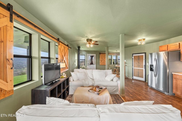 living room with a barn door, ceiling fan, dark wood-style floors, and a wealth of natural light