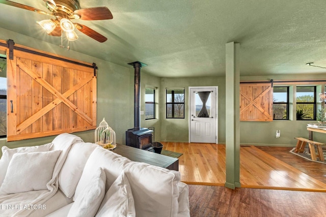 living room with a wood stove, a ceiling fan, wood finished floors, and a barn door