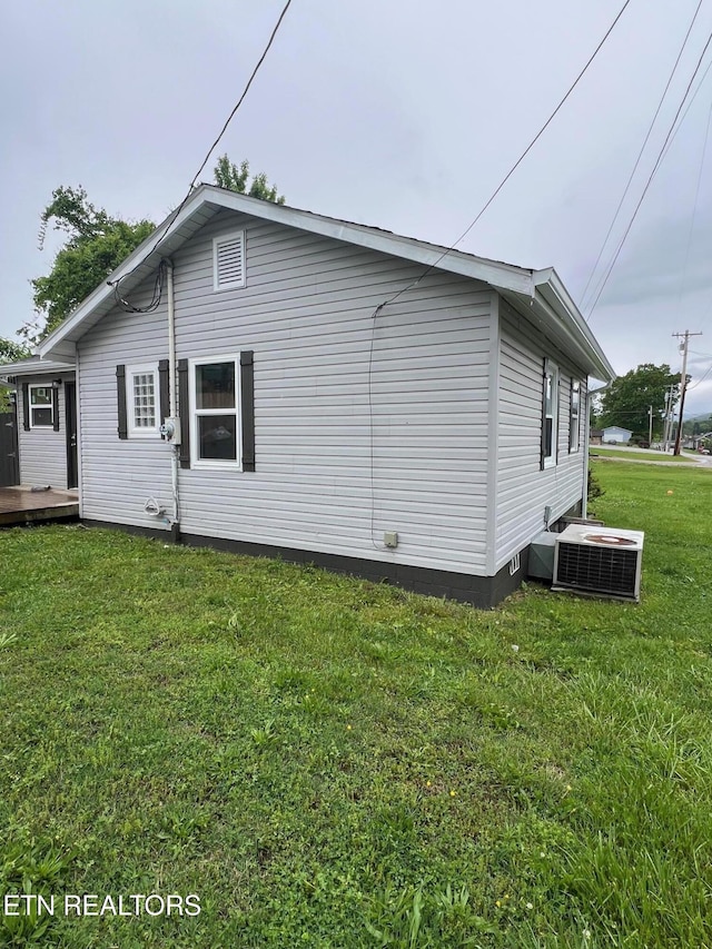 rear view of house with central AC unit, a deck, and a lawn