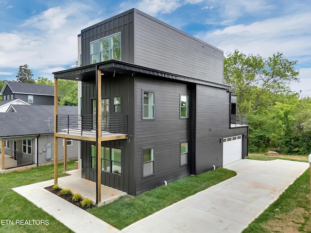 view of side of property with a garage, board and batten siding, concrete driveway, a balcony, and a lawn