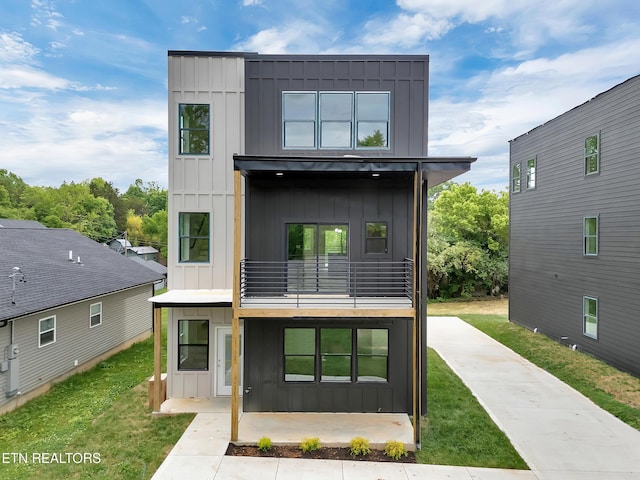 rear view of property with board and batten siding, a yard, and a balcony