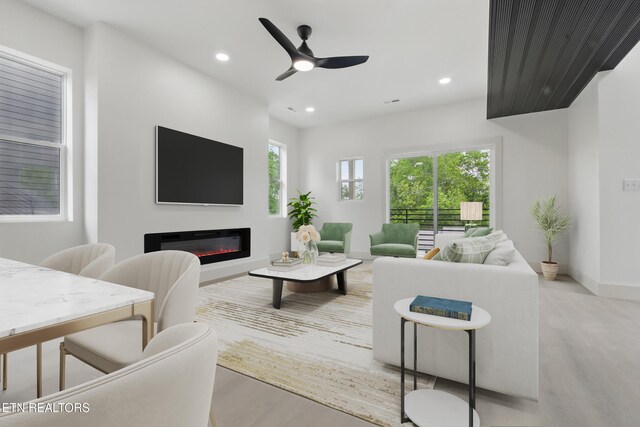 living room featuring ceiling fan, baseboards, light wood finished floors, a glass covered fireplace, and recessed lighting