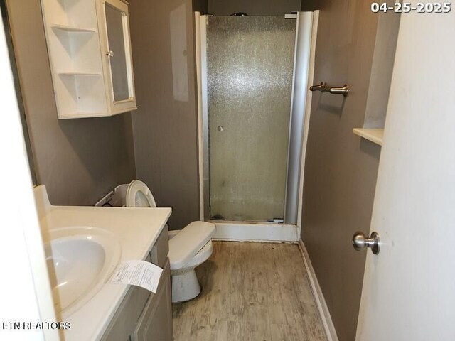 bathroom featuring a shower stall, wood finished floors, vanity, baseboards, and toilet