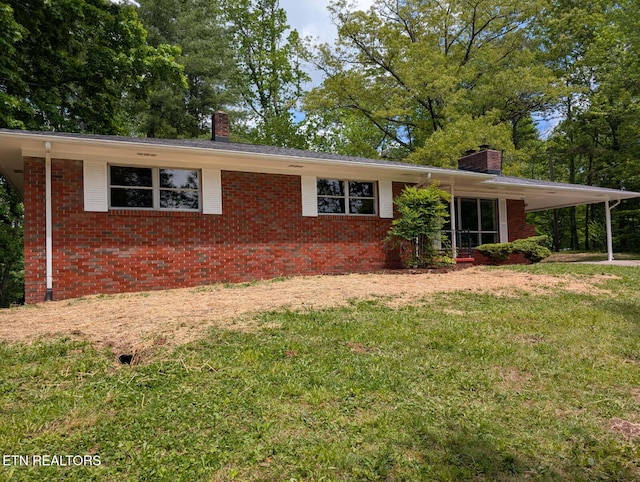 ranch-style house featuring a carport, a chimney, brick siding, and a front yard