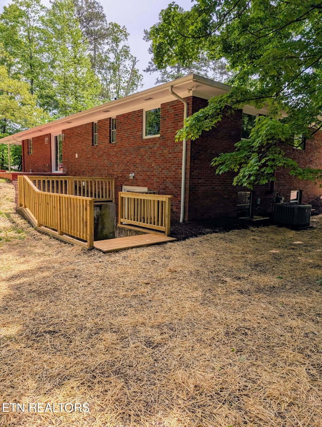 back of house with central air condition unit, brick siding, and a wooden deck