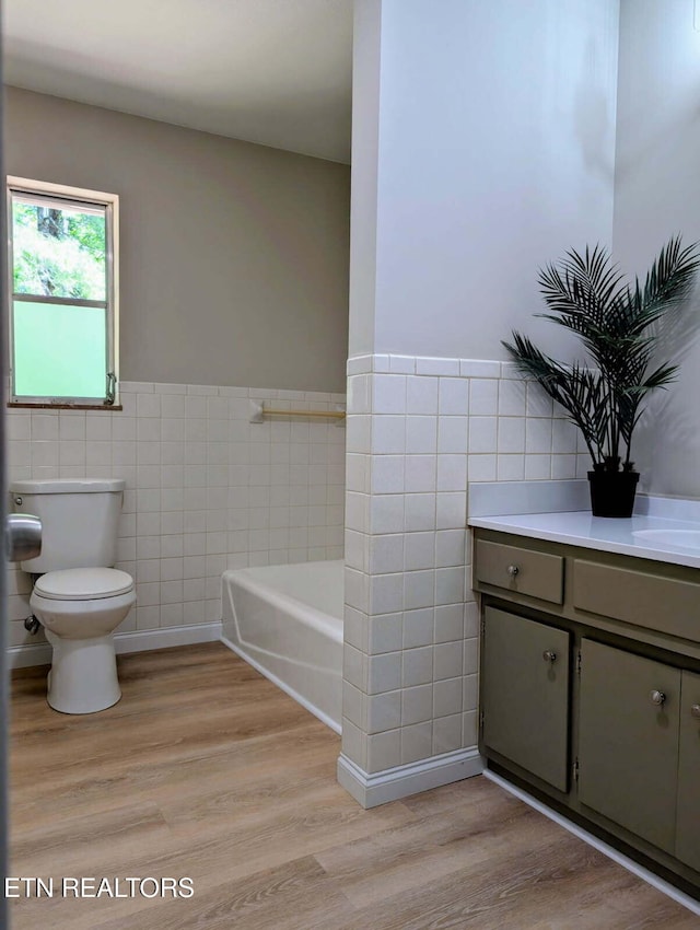 bathroom with wood finished floors, a bath, toilet, and tile walls