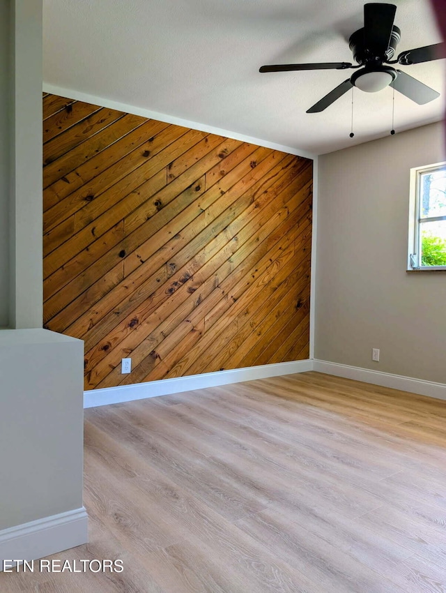 empty room featuring wooden walls, baseboards, ceiling fan, and wood finished floors