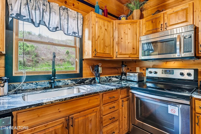 kitchen featuring brown cabinetry, dark stone counters, appliances with stainless steel finishes, and a sink