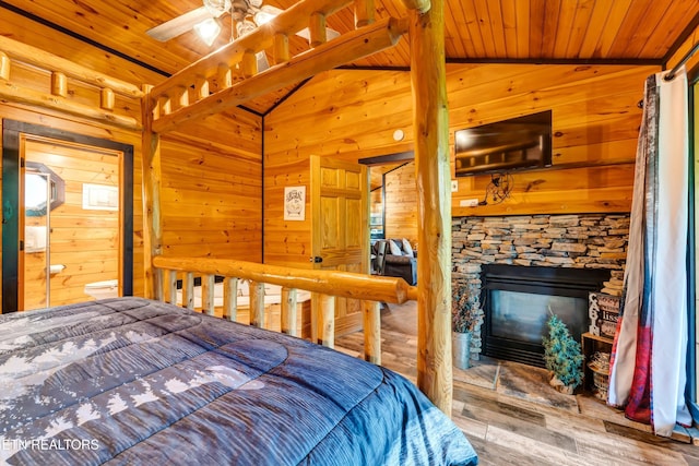 bedroom with vaulted ceiling, a stone fireplace, wood ceiling, wood walls, and wood finished floors