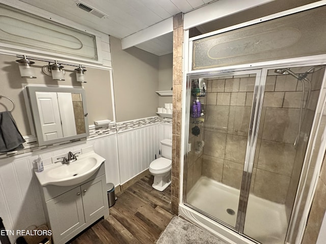 bathroom featuring toilet, wood finished floors, a stall shower, visible vents, and wainscoting