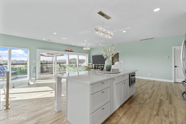 kitchen featuring light wood-style floors, light countertops, a chandelier, a center island, and pendant lighting