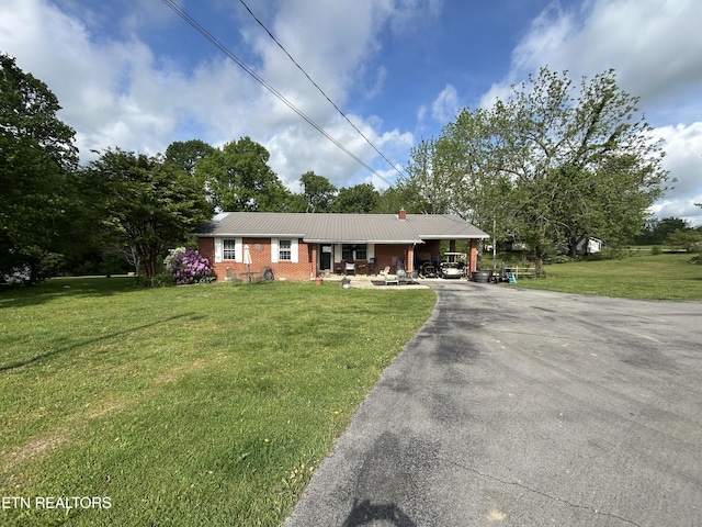 ranch-style house with brick siding, a front yard, a carport, driveway, and metal roof