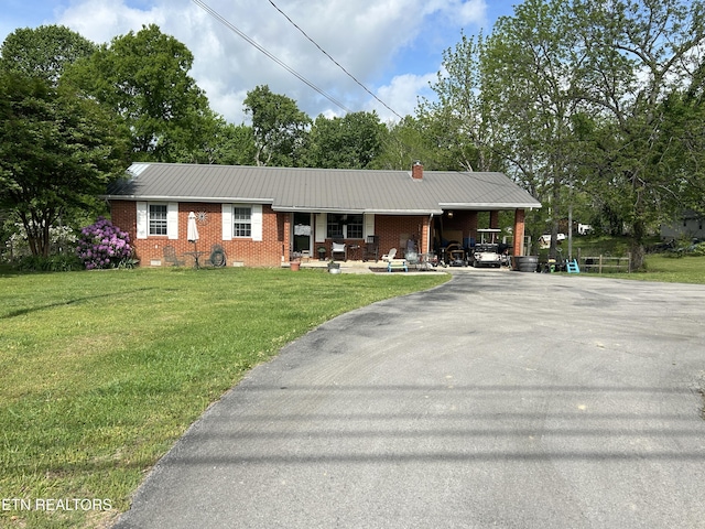 ranch-style home featuring a front yard, brick siding, metal roof, a porch, and driveway