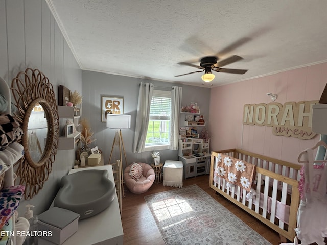 bedroom with a nursery area, ornamental molding, and wood finished floors
