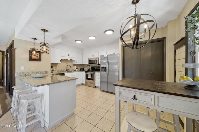 kitchen featuring appliances with stainless steel finishes, a sink, a peninsula, a chandelier, and white cabinetry