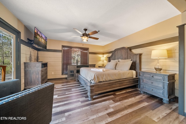 bedroom with wooden walls, a ceiling fan, and wood finished floors