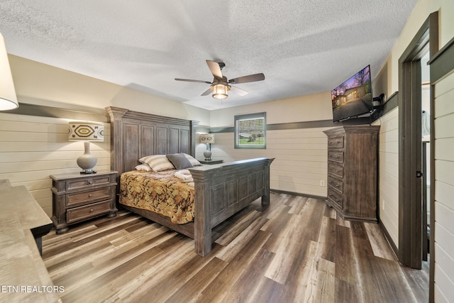 bedroom featuring ceiling fan, a textured ceiling, wood walls, and wood finished floors