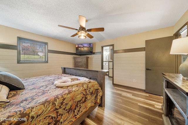bedroom with a ceiling fan, a textured ceiling, wood walls, and wood finished floors