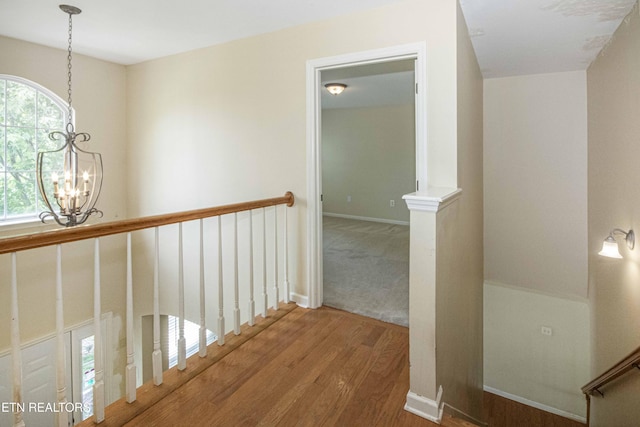 hall with an inviting chandelier, baseboards, an upstairs landing, and wood finished floors