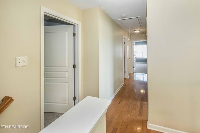 hallway featuring attic access, baseboards, and wood finished floors